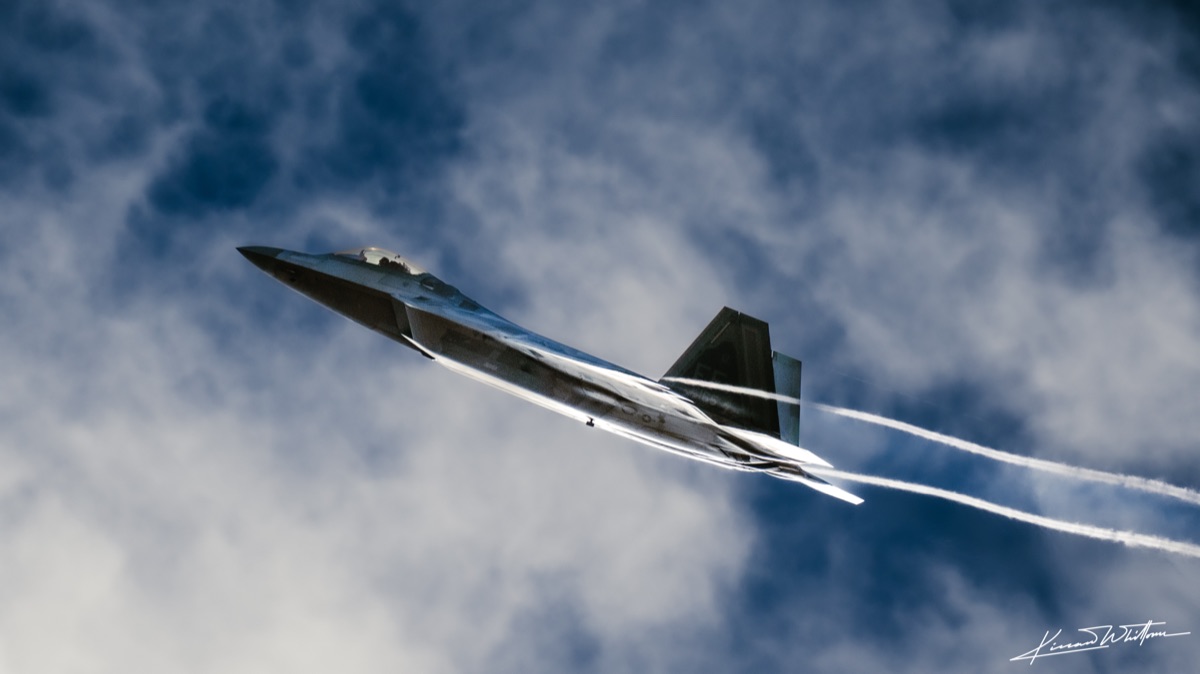 F-22 Raptor banking through clouds with vapor trails