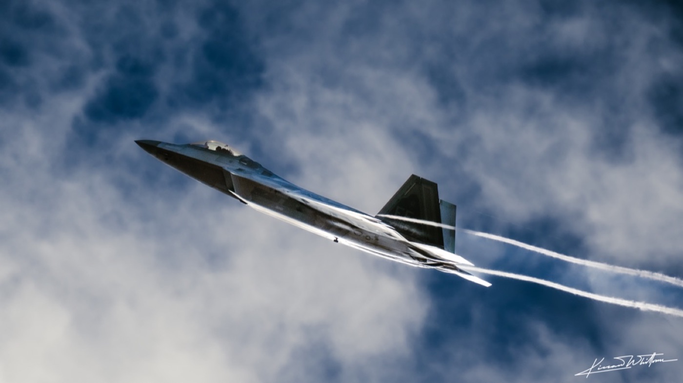F-22 Raptor banking through cloud with vapour trails